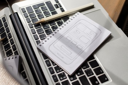 Silver laptop, sketchbook and pencil on the tableの写真素材