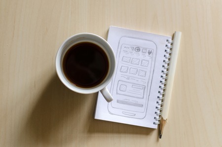 Cup of coffee, sketchbook and pencil laying on the tableの写真素材