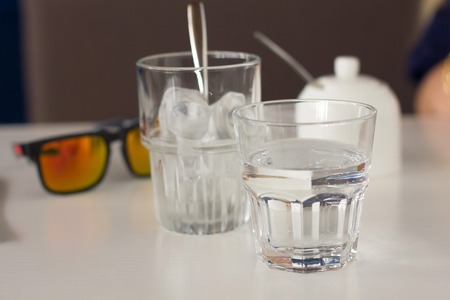 close up of eye glasses and twoglasses of water on the tableの写真素材