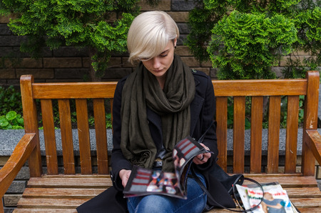 Young woman reading magazine on the bench in the cityの写真素材