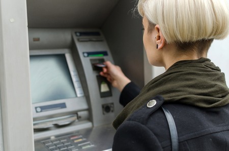 Young blonde woman using cash machine on the streetの写真素材