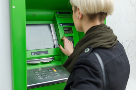 Young blonde woman using cash machine on the streetの写真素材
