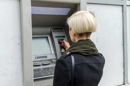 Young blonde woman using cash machine on the streetの写真素材