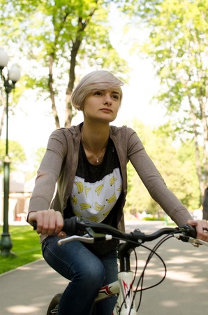 Young beautiful girl riding a white bicycle in the parkの写真素材