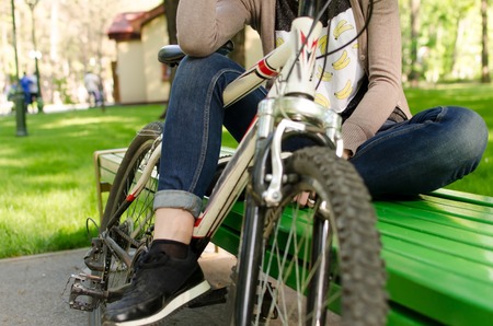 Young beautiful girl sitting on the bench near the white bicycle in the parkの写真素材