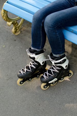 Young girl sitting on the bench wearing black rollers in the park