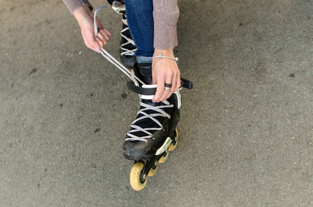 Young girl ties shoelaces on black rollers in the parkの写真素材