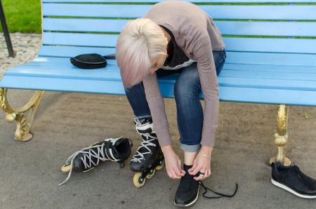 Young girl ties shoelaces on black rollers in the parkの写真素材