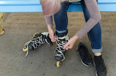 Young girl ties shoelaces on black rollers in the parkの写真素材