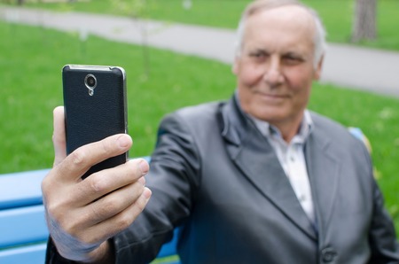 Aged man is using his cellphone in the parkの写真素材