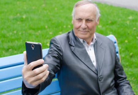 Aged man is using his cellphone in the parkの写真素材