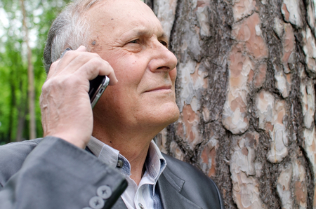 Aged man is using his cellphone in the parkの写真素材
