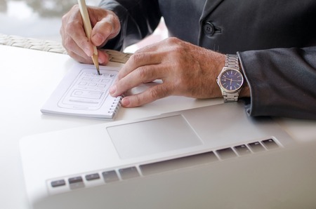 Aged man is making notes in the notebook in the parkの写真素材