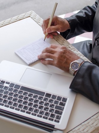 Aged man is making notes in the notebook in the parkの写真素材