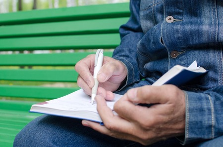 Aged man is making notes in the daily planner in the park