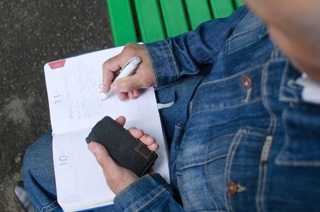 Aged man is making notes in the daily planner
