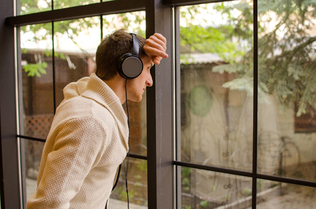 Young man in headphones is listening music beside the windowの写真素材