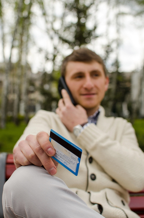 Young man is talking on the phone with blue card in right handの写真素材