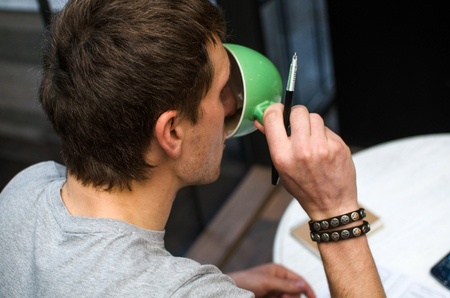 Young man drinking coffee from the green cup in the cafeの写真素材