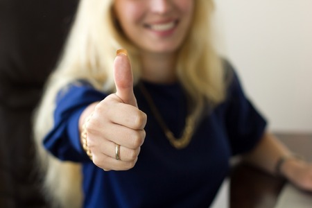 Young blonde woman with thumb up in the officeの写真素材