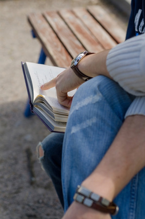 Young man is helping teenager to read a book in the parkの写真素材
