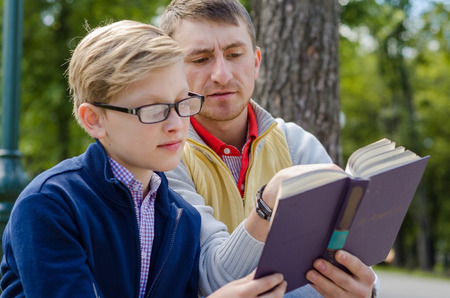 Young man is helping teenager to read a book in the parkの写真素材