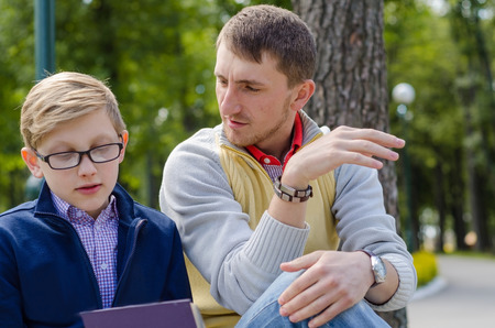 Young man is helping teenager to read a book in the parkの写真素材