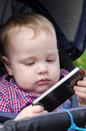 Small baby boy is playing with the cellphone in the parkの写真素材