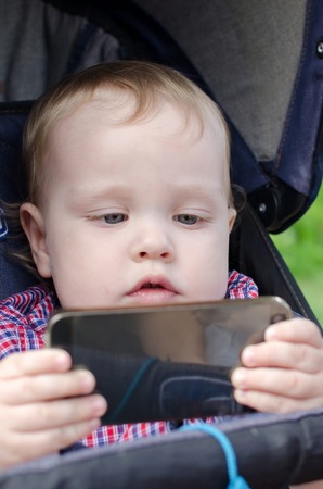 Small baby boy is playing with the cellphone in the parkの写真素材