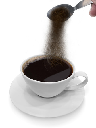 Hand pours instant coffee from a spoon in a coffee cupの写真素材