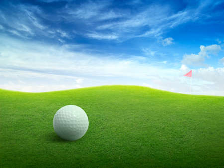 Close up golf ball on green grass field and red golf flag on green fairway with beautiful blue skyの写真素材