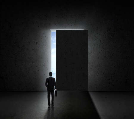 Businessman walking in go of bright big shining door in a concrete wall with a view to the city