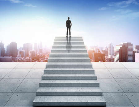 Vision concept. Successful businessman standing on staircase and looking over cityの写真素材