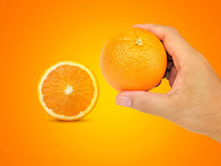 hand holding orange fruit and orange slices on orange backgroundの写真素材
