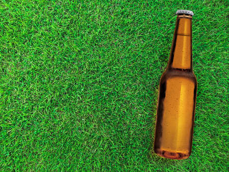 Beer bottle with water drops on green field of grass backgroundの写真素材