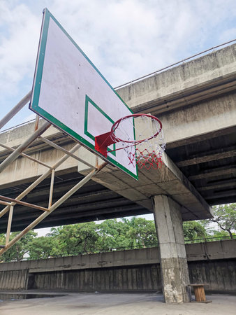 Empty sunlit basketball court in city park on hot sunny day under blue zenith sky. Bright sun in the...