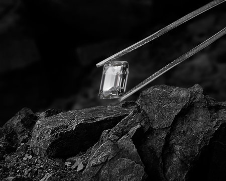 Cut Beautiful diamond held by tweezers on black coal backgroundの写真素材