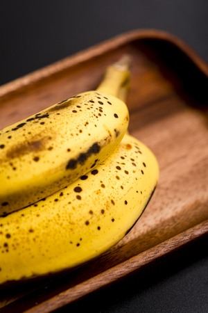 Two organic bananas in a wood sish over a black board.の写真素材