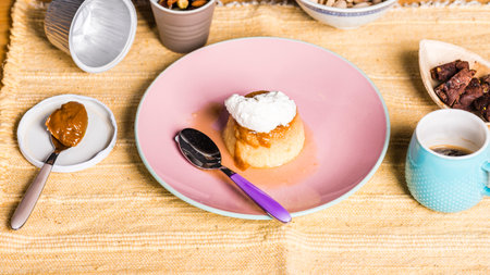 Flan -  creme on top, on a pink plate over a wooden board, served with chocolate cookies, dulce de leche confection , coffee and nuts.の写真素材