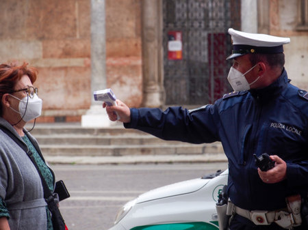 Cremona, Lombardy, Italy - 13 th may 2020 - Local police officer measuring adultÂ  woman body temperature with infrared thermometer scanner while in line to access open food marketのeditorial素材