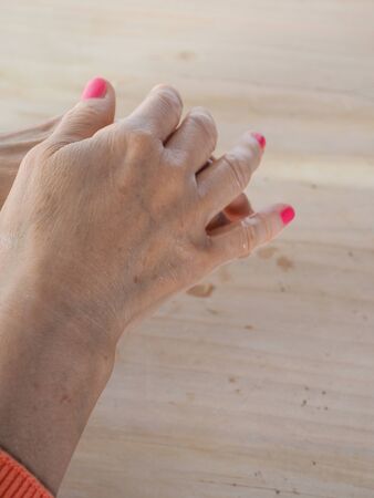 close up of  woman hands while cleaning and sanitizing  herself  with anti virus bacterial gel against covid-19 , fall dress, orange color over a wood table, earth tones.の写真素材