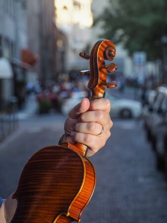 Male adult violinist hand holding antiquized handmade cremonese violin in the street at dawn in city street waiting to re start and play again in concert after coronavirus outbreaakの写真素材
