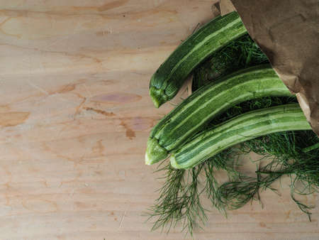 Overhead shot of a group of isolated three green biologic zucchini veggies fruit over a light brown table and a paper recycled bagwith copy spaceの写真素材