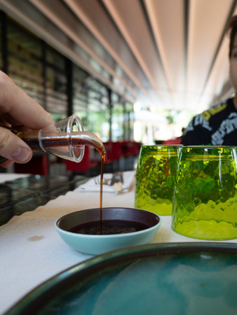 Hand pouring soy sauce from little jug into the bowl before eating asian food