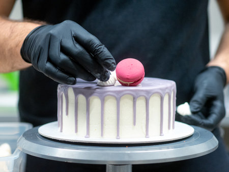frosted drip cake on stand while designer works on toppingの写真素材