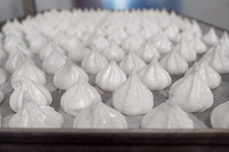 pastry chef baker artisan making white swirl and twirl meringue cones with piping bag filled with...
