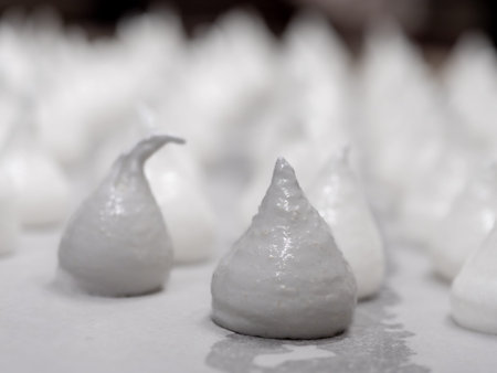 pastry chef baker artisan making white swirl and twirl meringue cones with piping bag filled with egg cream and sugar to bake for sweet preparationの写真素材