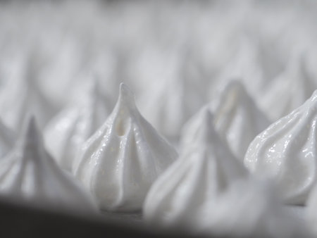 pastry chef baker artisan making white swirl and twirl meringue cones with piping bag filled with egg cream and sugar to bake for sweet preparationの写真素材