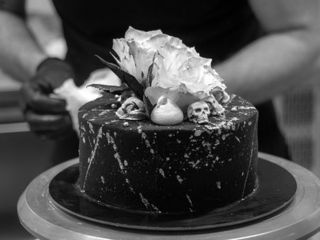 pastry chef baker topping birthday black airbrush painted frosted cake, two real roses silver sprayed and edible chocolate skull toppers, silver brush strokesの写真素材