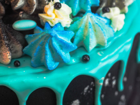frosted black painted cup cake with blue turquoise dripping and colored handmade meringue topping studio white isolated backgroundの写真素材